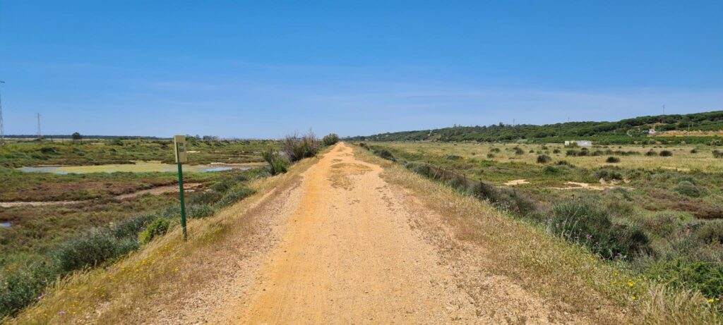 Verlaten gravelweg in Spanje. De omgeving is desolaat met weinig begroeiing. De weg is geel en de lucht is blauw.